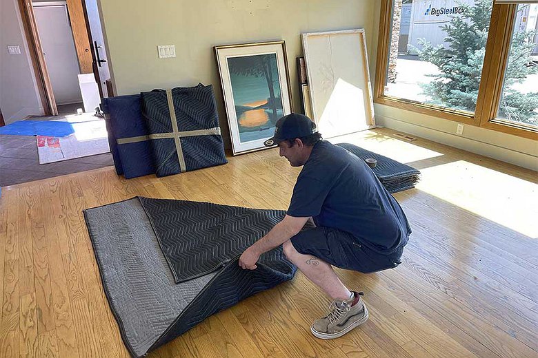 Mover wrapping furniture with protective moving blankets in a home