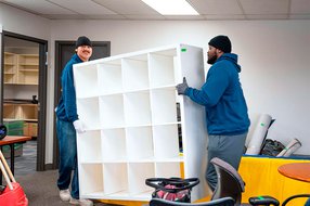 Two professional movers carrying a large white shelving unit inside an office during a move in Calgary