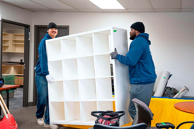 Two professional movers carrying a large white shelving unit inside an office during a move in Calgary